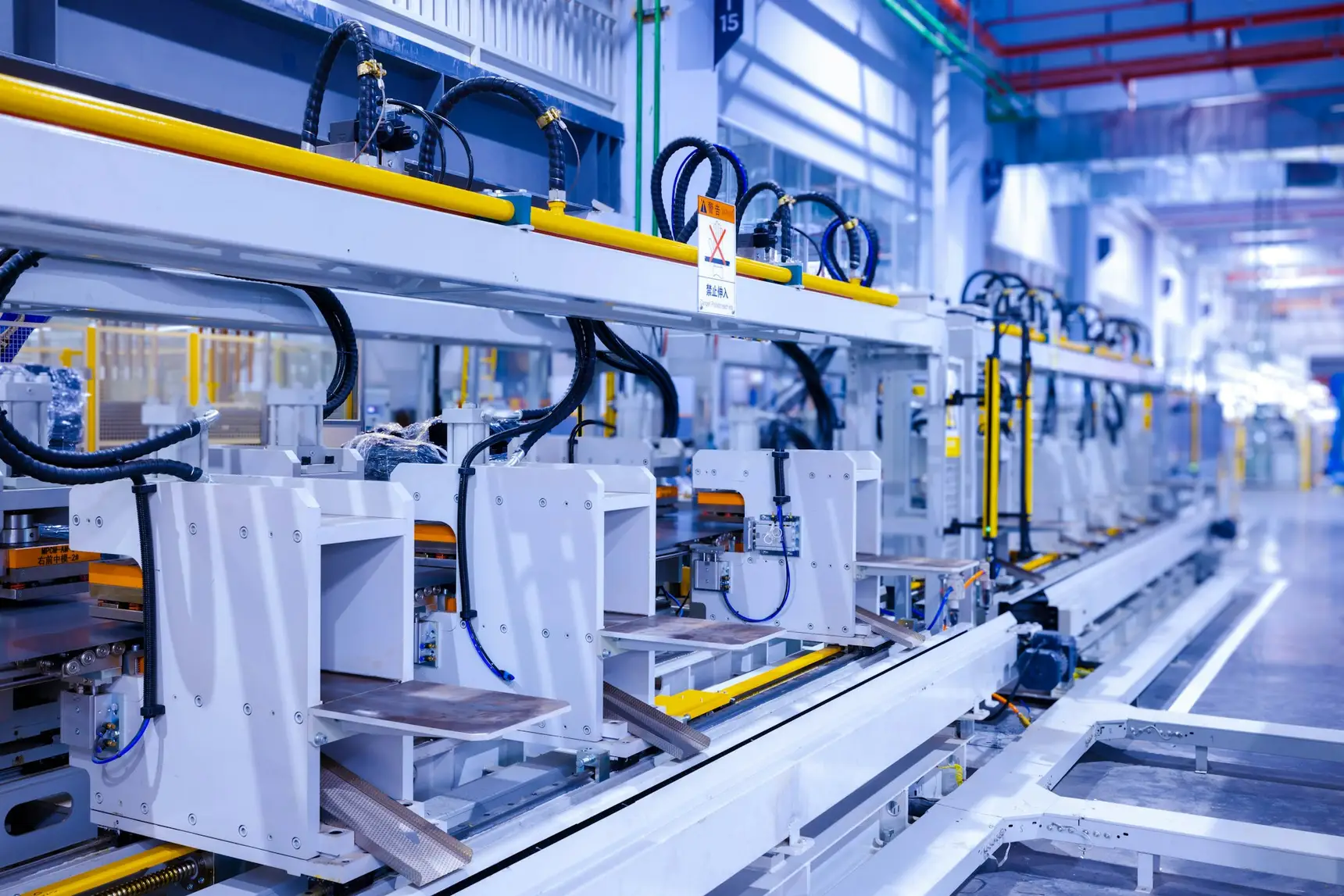 A production line inside a Chinese factory, machines in a row along a rail with safety signage in Chinese above them
