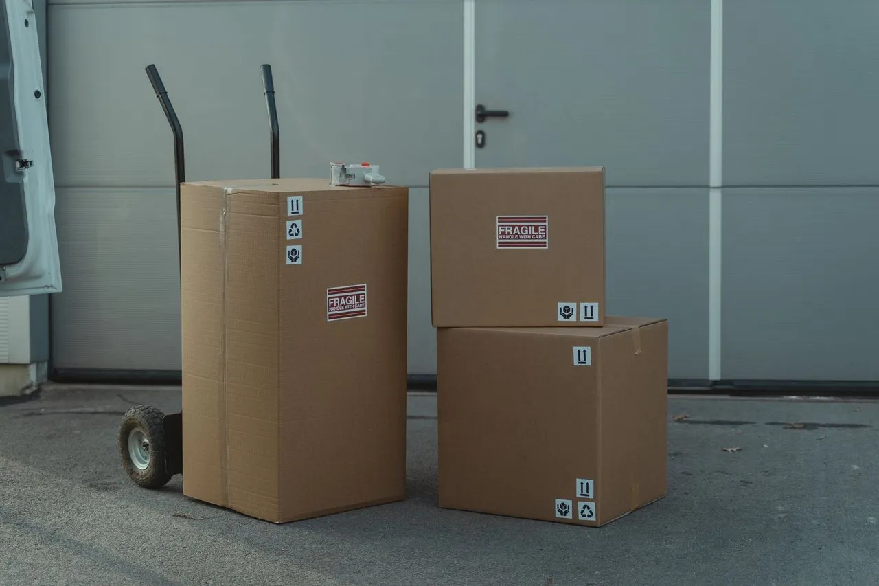 Three cartons on a hand truck beside an open van, marked fragile with handling arrows.